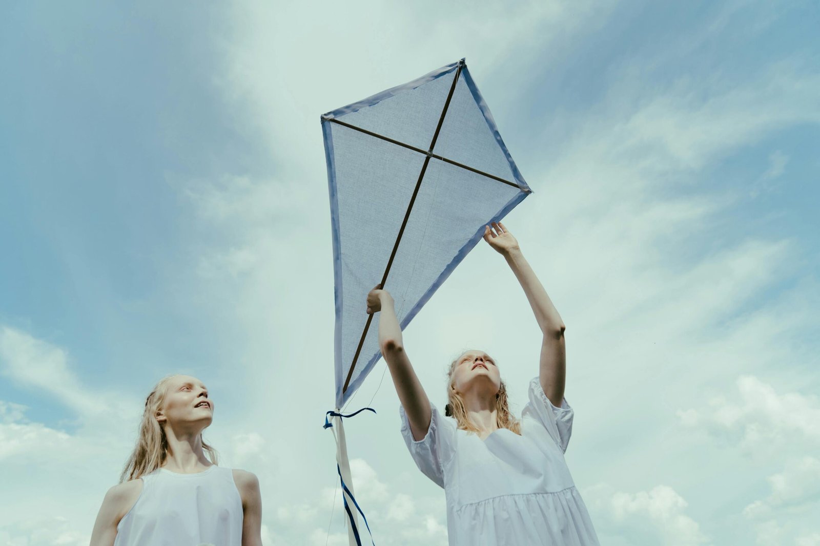 Two young adult caucasian women flying a kite together under a clear blue sky. Captured outdoors.