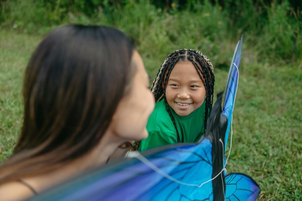 Two girls with braided hair enjoy a sunny day flying a kite in a lush green park.